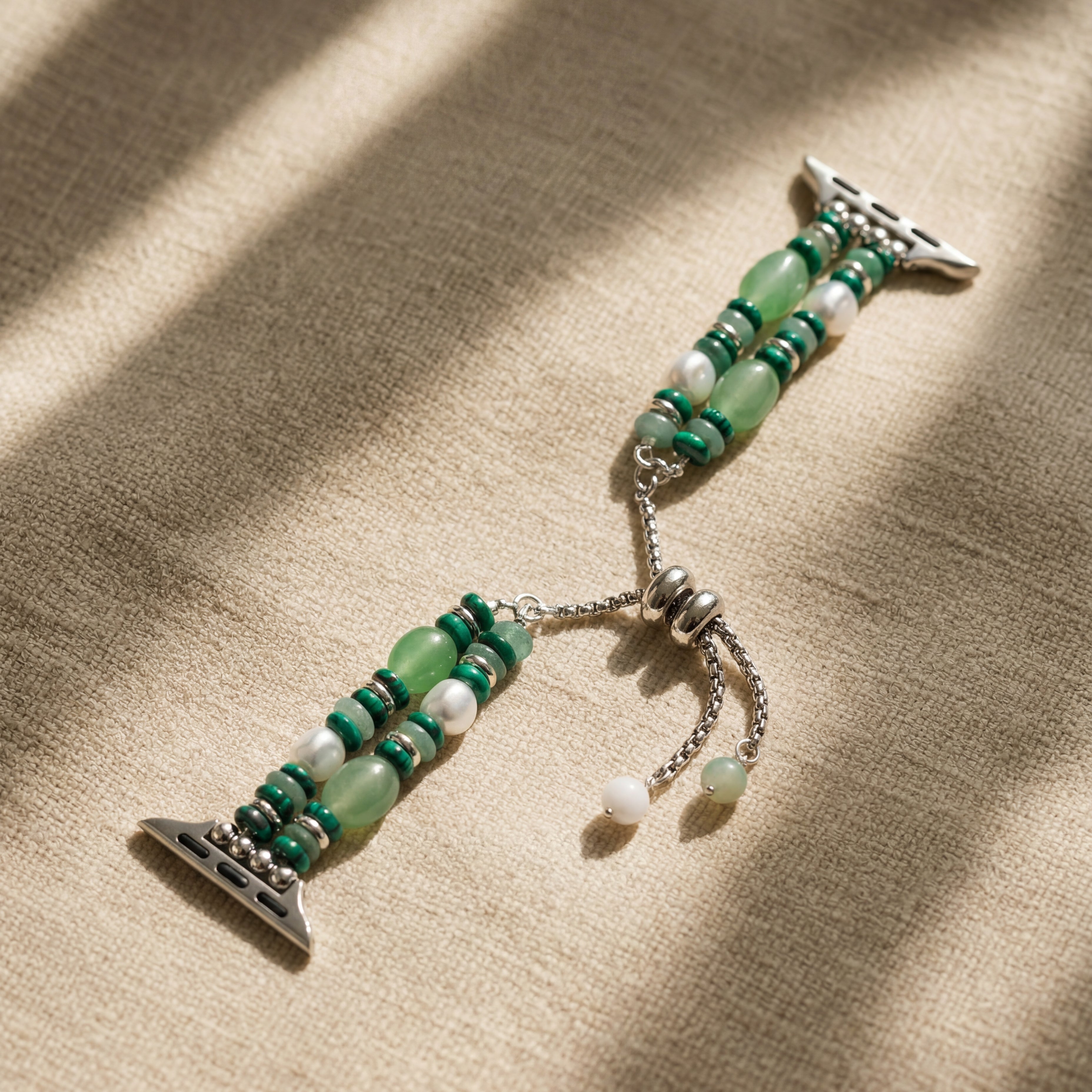Green beaded bracelet with silver charms on a beige fabric background